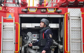 Ein Feuerwehrmann in Schutzausrüstung steht an einem offenen Fach eines Feuerwehrfahrzeugs in der Ukraine