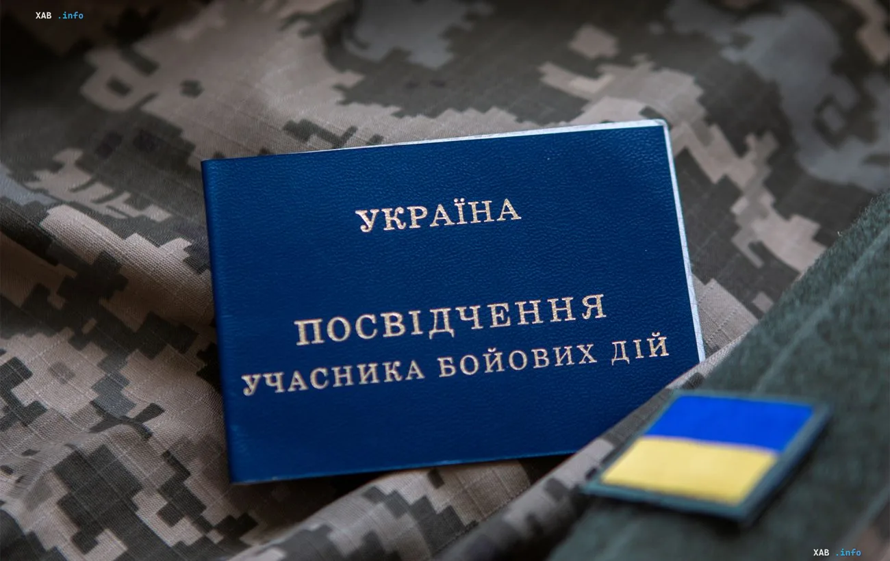 Синее удостоверение участника боевых действий Украины на камуфляжном фоне рядом с шевроном