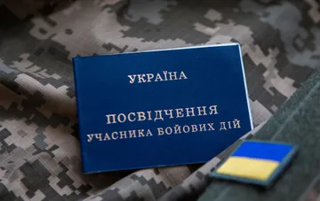 Синее удостоверение участника боевых действий Украины на камуфляжном фоне рядом с шевроном