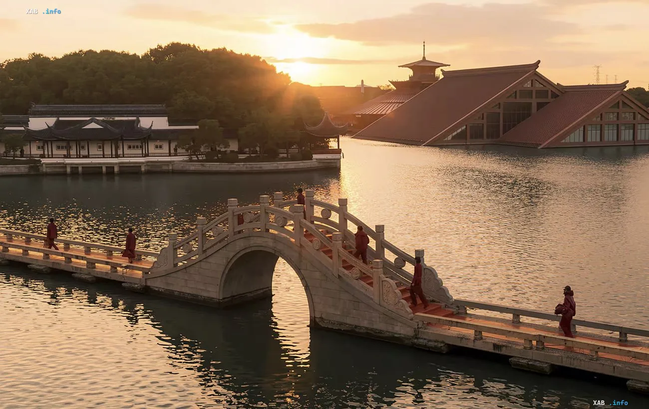 Menschen in roter Kleidung gehen bei Sonnenuntergang über eine Bogenbrücke in einem chinesischen Garten inmitten traditioneller Architektur