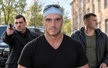 Три мужчины в темной одежде, включая актера в бандане, во время съемок криминального сериала