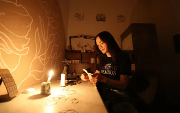 Дівчина сидить за столом при свічках у темній кімнаті, працюючи з паперами