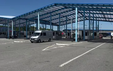 Автомобильный пункт пропуска с синим навесом и микроавтобусом под ним на фоне ясного неба