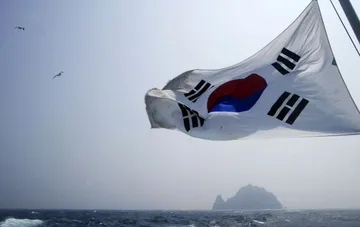 Südkoreanische Flagge weht im Wind vor einer Meereslandschaft und einer fernen Felseninsel