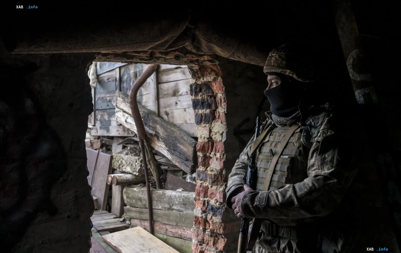 Військовослужбовець у камуфляжі та захисній масці спостерігає зі зруйнованого укриття на передовій