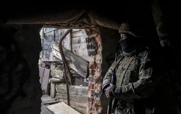 Військовослужбовець у камуфляжі та захисній масці спостерігає зі зруйнованого укриття на передовій