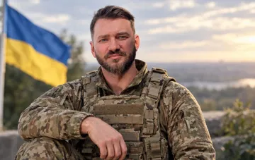 Украинский хореограф и военнослужащий ВСУ Дмитрий Дикусар в военной форме на фоне флага Украины