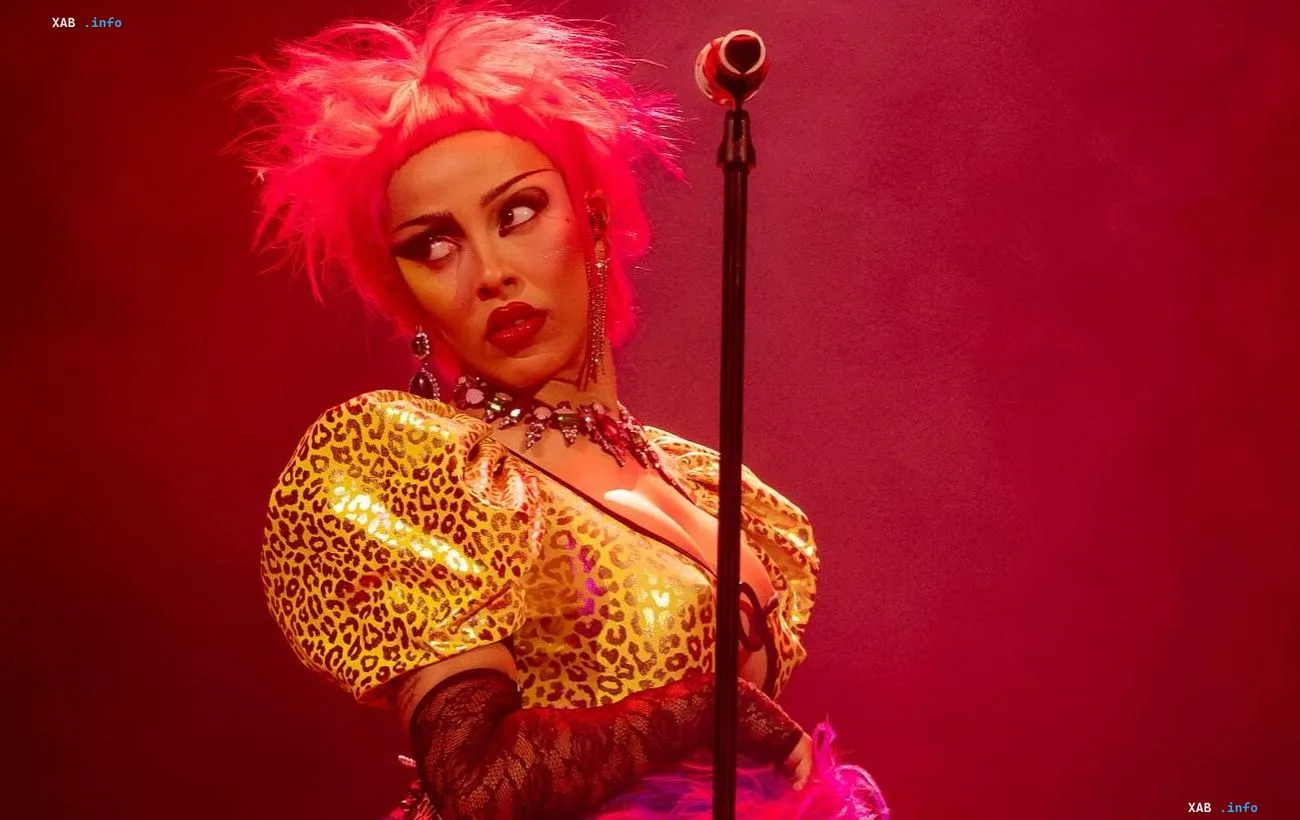 Singer Doja Cat in a bright stage outfit with pink hair against a red light