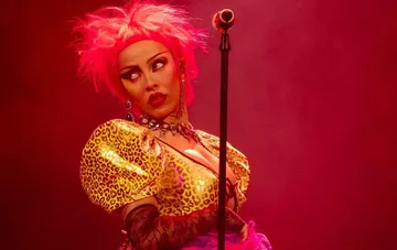 Singer Doja Cat in a bright stage outfit with pink hair against a red light