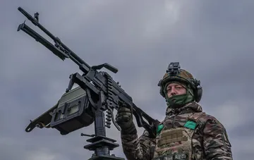 Украинский военнослужащий в экипировке у пулеметной установки крупным планом во время боевого дежурства