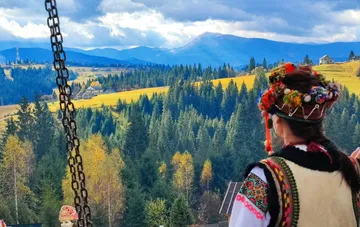 Женщина в традиционном карпатском костюме смотрит на осенние горы с видом на вершины и хвойный лес