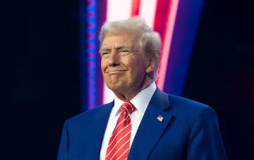 US President Donald Trump speaking during a public event against blue and red decorations