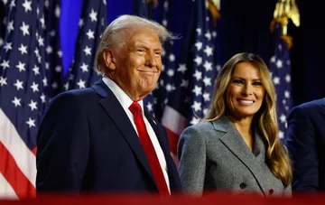 US President Donald Trump and First Lady Melania Trump smiling in front of American flags during an event