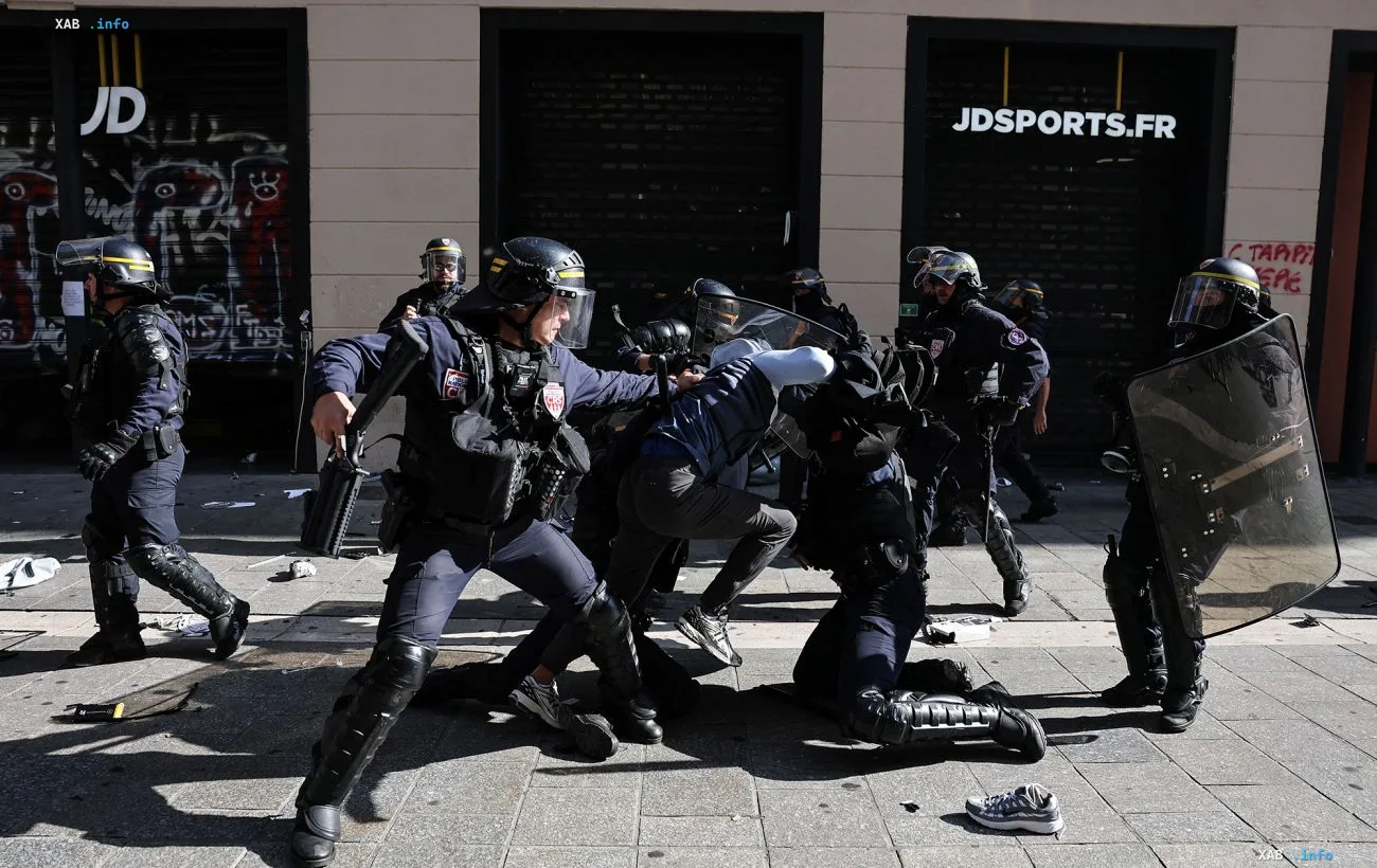 French police officers in protective gear detain a street protest participant on a city street