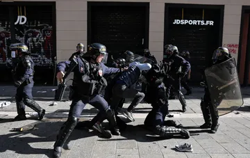French police officers in protective gear detain a street protest participant on a city street