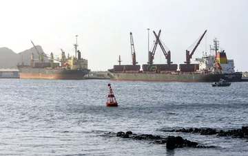 Грузовые судна и танкеры стоят в порту на фоне моря и гор