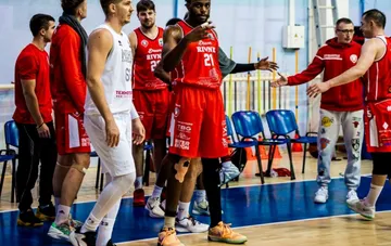 Basketball players in red and white uniforms communicating and shaking hands on a sports hall court