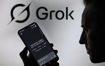 Мужчина смотрит на экран смартфона с чат-ботом Grok и логотипом компании на фоне