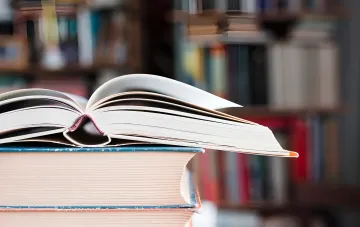 Открытая книга лежит на стопке книг на фоне размытых книжных полок