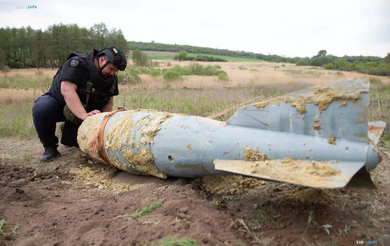 Ein Militärspezialist inspiziert die Trümmer einer großen gelenkten Fliegerbombe mit Heckflossen im Gelände