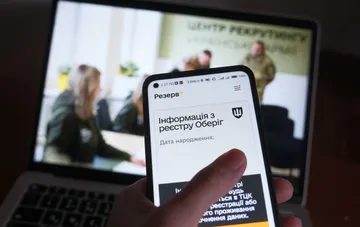 Смартфон с открытым приложением Резерв+ на фоне ноутбука в помещении