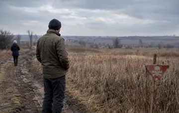 Мужчина со спины смотрит на поле в Украине с предупреждающим знаком о минах