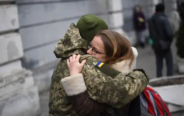 Украинский военный в камуфляжной форме крепко обнимает близкого человека на улице города