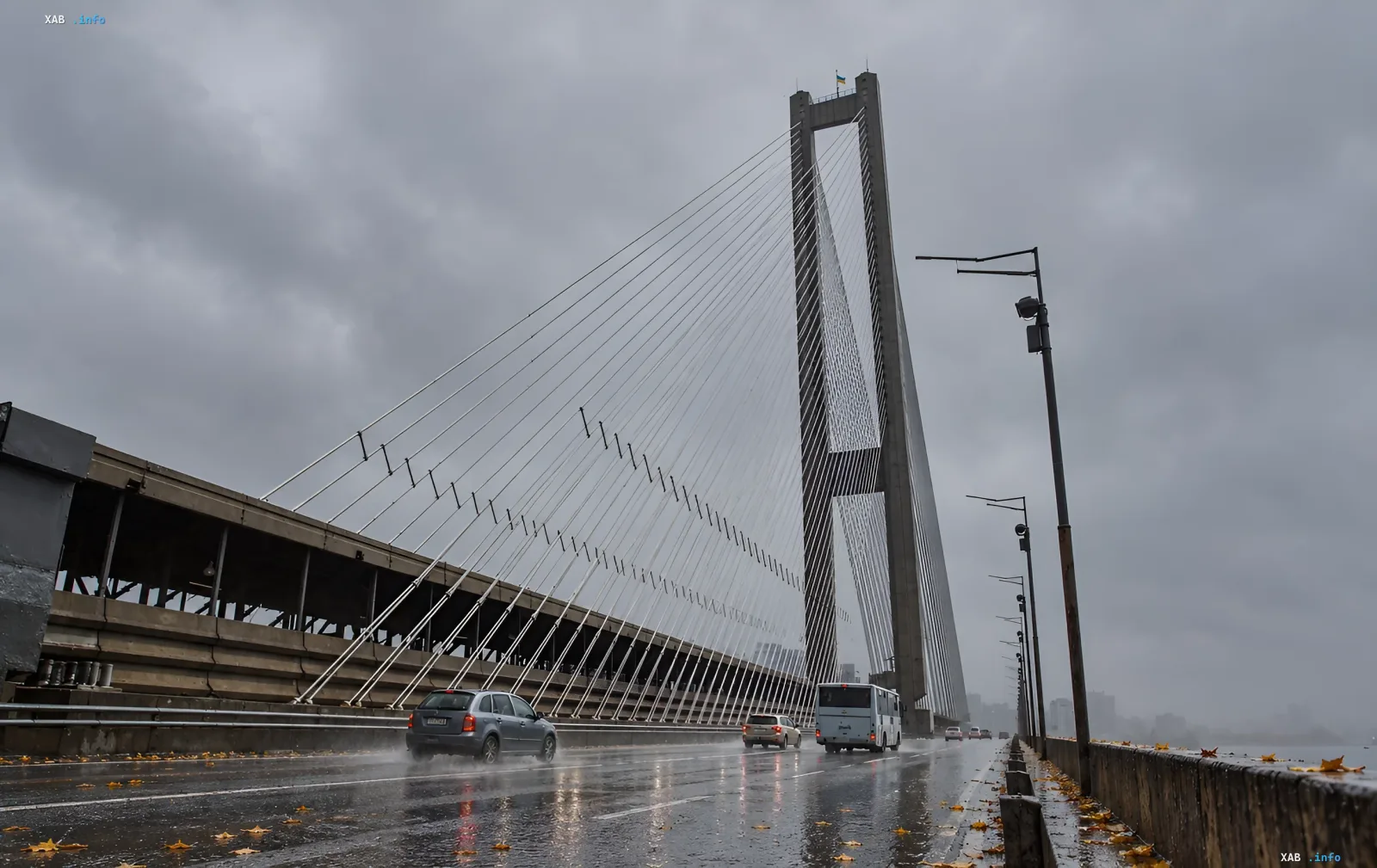 Автомобили едут по мосту в дождливую погоду под серым небом в Киеве