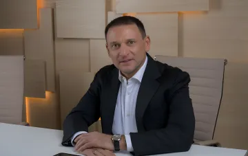 Дмитрий Добкин в деловом костюме за светлым столом в светлом офисе с деревянными панелями на стене