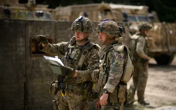 Two British soldiers in camouflage gear reviewing documents and a map during field exercises