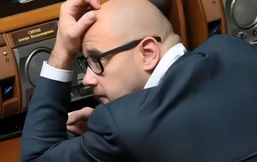 Чоловік у окулярах сидить за столом і тримається за голову під час засідання в українському парламенті