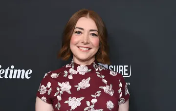 Schauspielerin Alyson Hannigan lächelt bei einer Veranstaltung in einem bordeauxroten Blumenkleid.