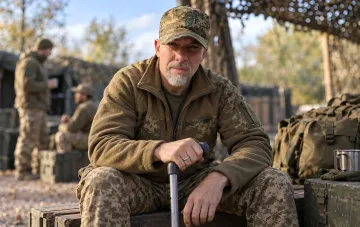 Український актор і військовослужбовець Геннадій Попенко у камуфляжі з ціпком у польовому таборі