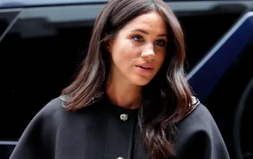 Meghan Markle wearing a dark coat with a collar during television filming