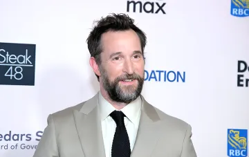 Actor Noah Wyle smiling at a press event in a suit and tie