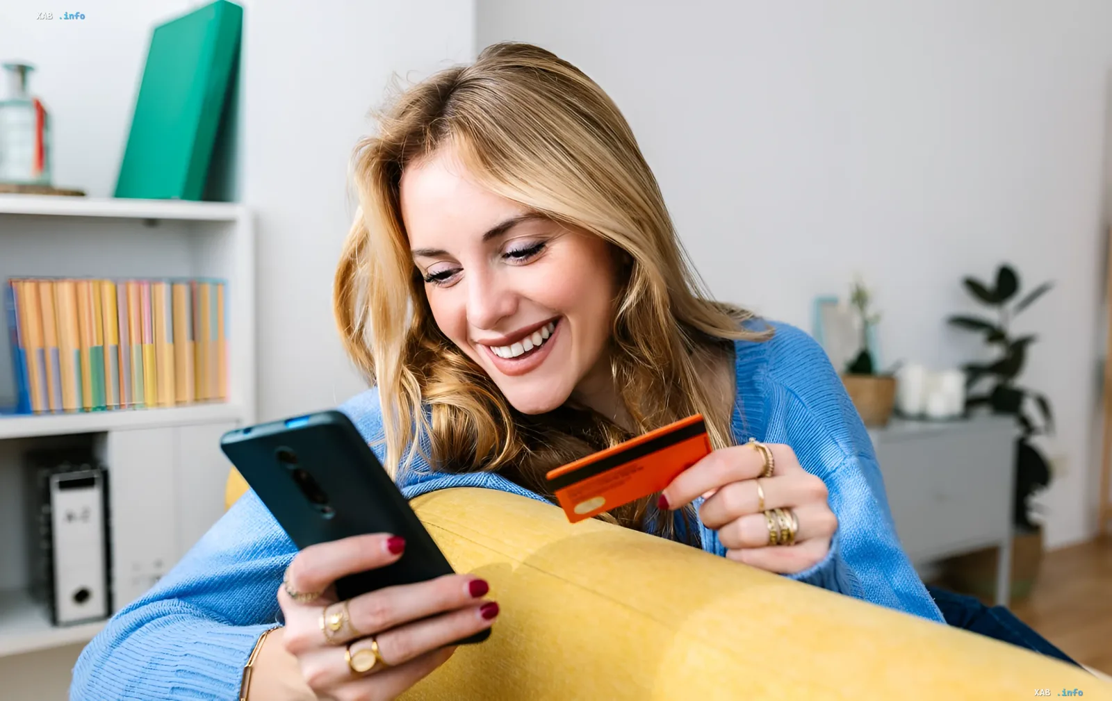 Smiling woman holding a smartphone and credit card while sitting at home