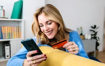 Smiling woman holding a smartphone and credit card while sitting at home