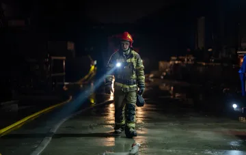 Firefighter in protective gear with a flashlight patrolling a night street after a strike in Kharkiv