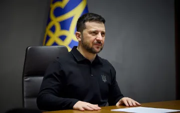 Президент Украины Владимир Зеленский в черной футболке сидит за столом во время выступления.