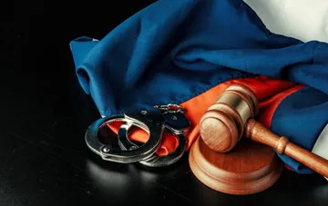 Gavel and handcuffs on a flag background on a desk in a courtroom
