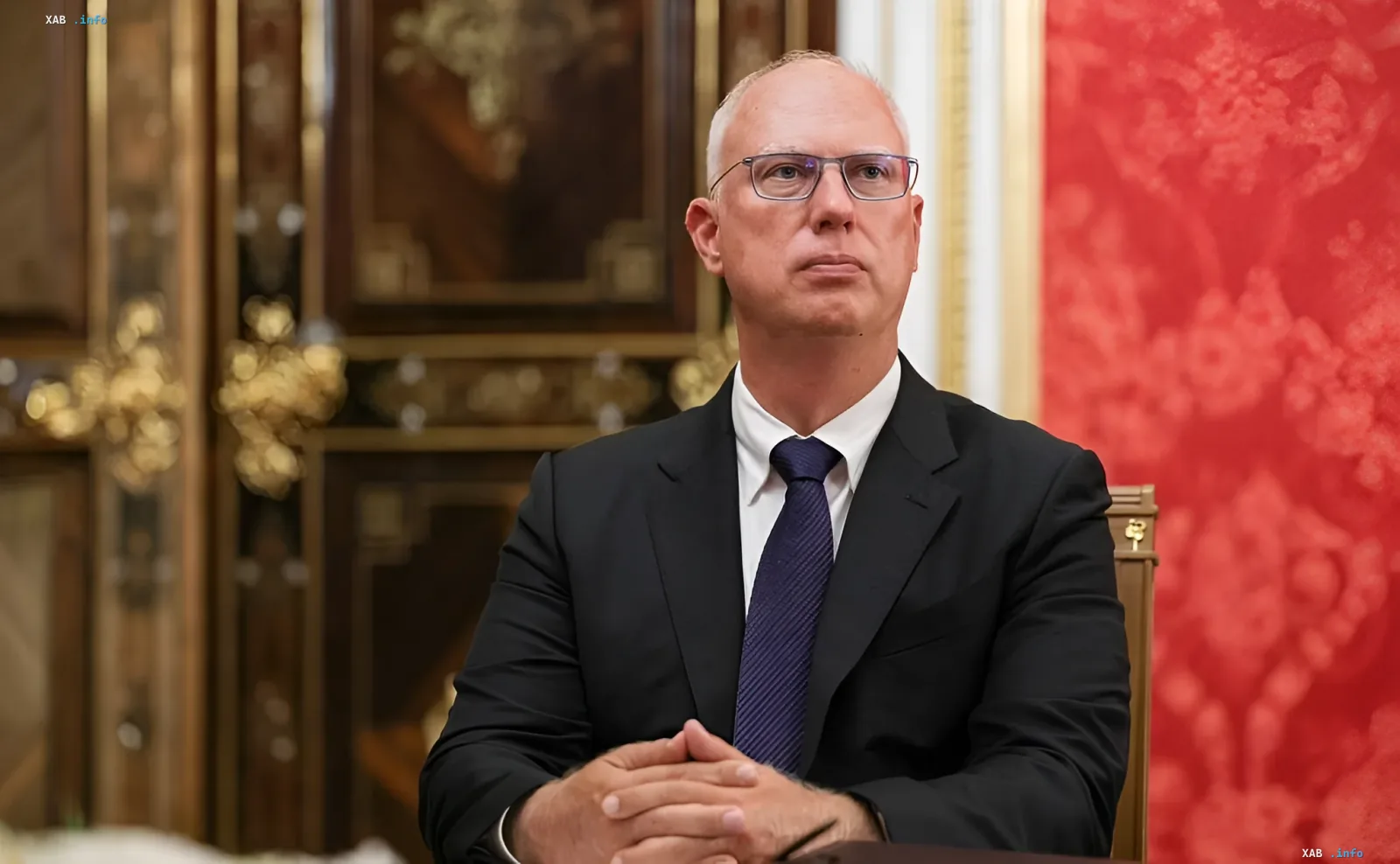 Специальный посланник президента РФ Кирилл Дмитриев в костюме за столом на фоне красной стены