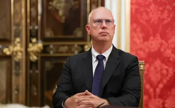 Специальный посланник президента РФ Кирилл Дмитриев в костюме за столом на фоне красной стены