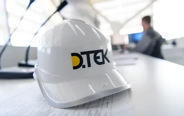 Белая строительная каска с логотипом DTEK на столе в светлом офисе энергетической компании