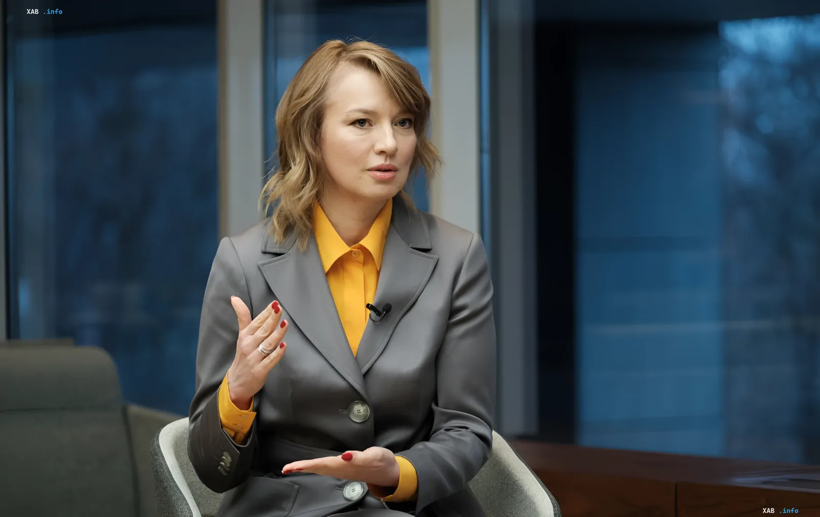 A woman in a business suit and yellow shirt giving an interview during a conversation