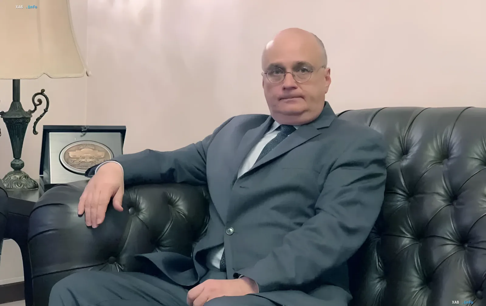 Russian diplomat Gleb Desyatnikov sitting in a suit on a leather sofa in an office