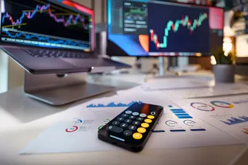 Графіки на моніторах та калькулятор на робочому столі для аналізу фінансових даних акцій