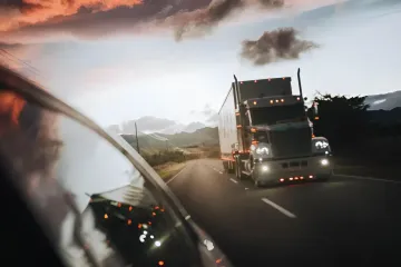Ein Lkw fährt bei Sonnenuntergang auf einer Autobahn neben einem Auto