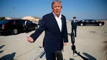 Дональд Трамп в темно-синем костюме дает интервью журналистам на аэродроме рядом с черными лимузинами
