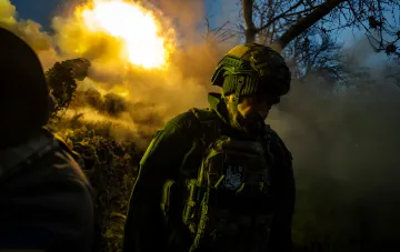 Украинский военнослужащий в каске и бронежилете на фоне взрыва и дыма на передовой