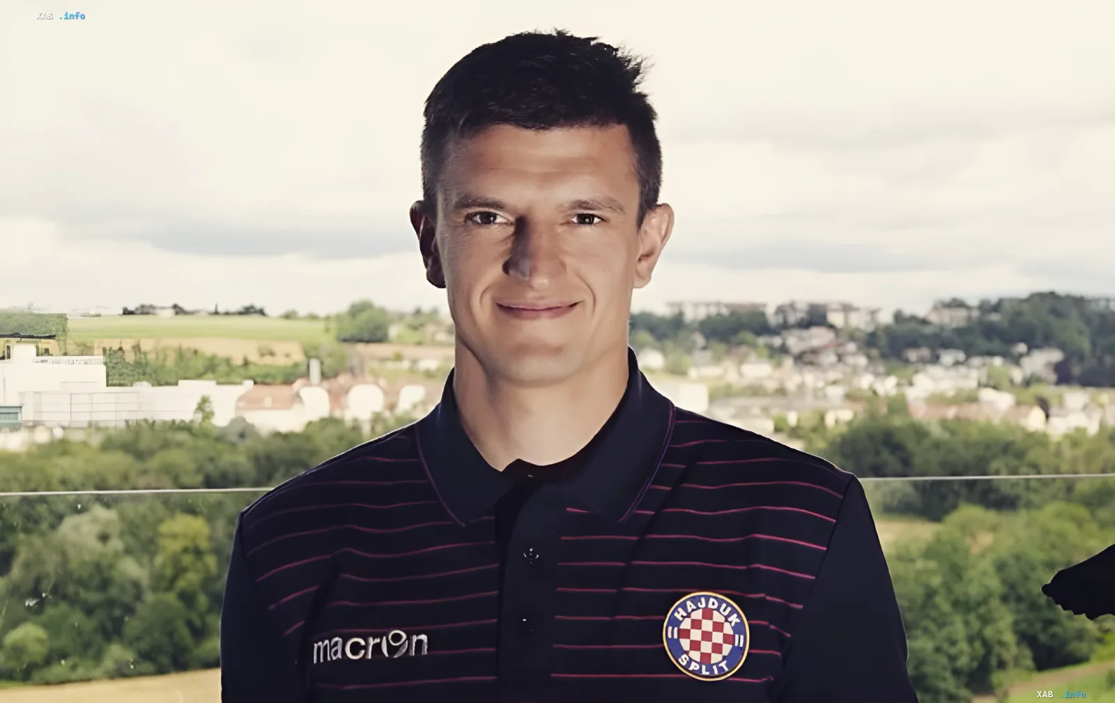 Der ukrainische Fußballspieler Maksym Bilyi lächelt in einem dunklen gestreiften Poloshirt mit Vereinswappen